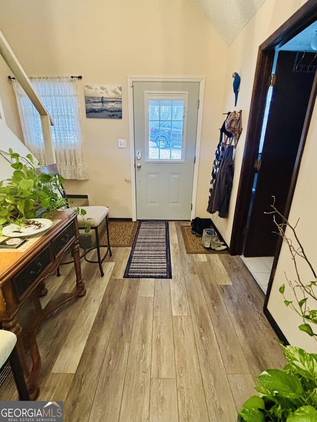 doorway to outside with lofted ceiling, light hardwood / wood-style floors, and a textured ceiling