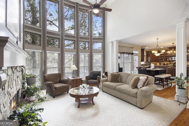 living room featuring ceiling fan with notable chandelier, a fireplace, decorative columns, and light wood-type flooring