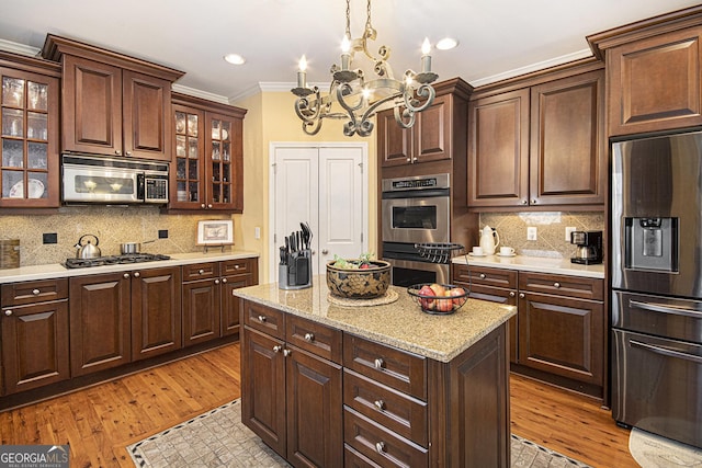 kitchen featuring pendant lighting, ornamental molding, stainless steel appliances, and light hardwood / wood-style flooring