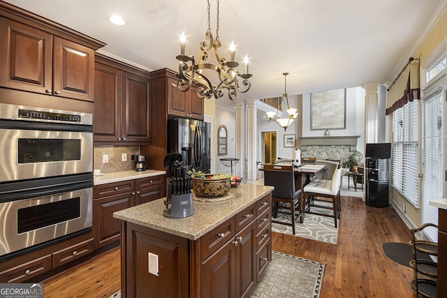 kitchen with pendant lighting, decorative columns, refrigerator with ice dispenser, a chandelier, and stainless steel double oven