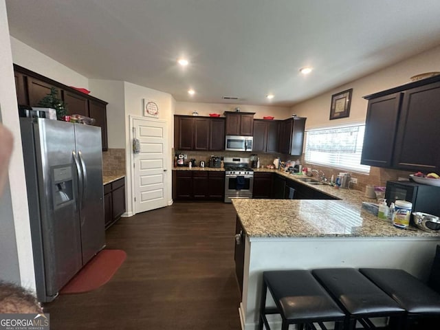 kitchen featuring dark brown cabinetry, stainless steel appliances, a peninsula, a sink, and decorative backsplash