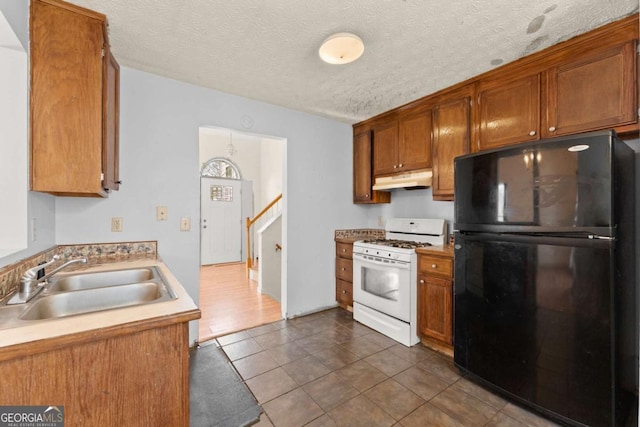 kitchen with sink, dark tile patterned floors, white range with gas cooktop, black fridge, and a textured ceiling