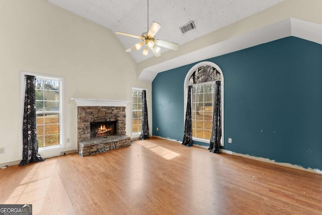 unfurnished living room with hardwood / wood-style flooring, a stone fireplace, high vaulted ceiling, and ceiling fan