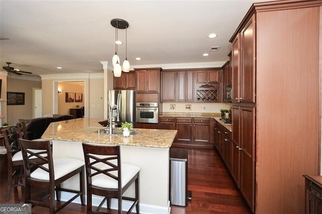 kitchen featuring dark hardwood / wood-style floors, decorative light fixtures, light stone counters, stainless steel appliances, and a center island with sink