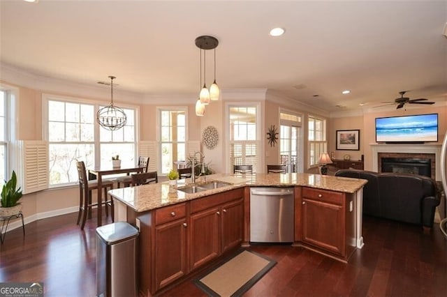 kitchen with pendant lighting, sink, stainless steel dishwasher, crown molding, and a center island with sink