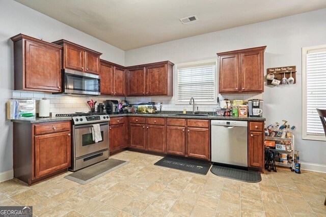 kitchen with stainless steel appliances, sink, decorative backsplash, and dark stone counters