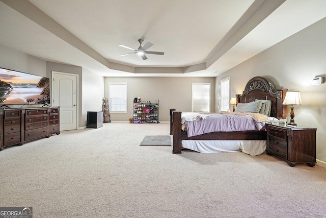 bedroom with a raised ceiling, ceiling fan, light colored carpet, and multiple windows