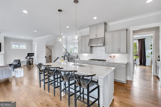 kitchen featuring a breakfast bar, sink, decorative light fixtures, a center island with sink, and light stone countertops