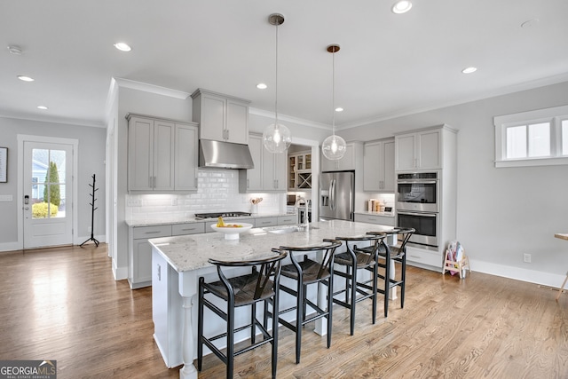 kitchen featuring a breakfast bar, sink, decorative light fixtures, a center island with sink, and appliances with stainless steel finishes