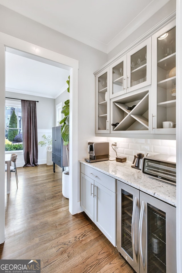 bar with white cabinets, beverage cooler, light stone counters, crown molding, and light hardwood / wood-style flooring