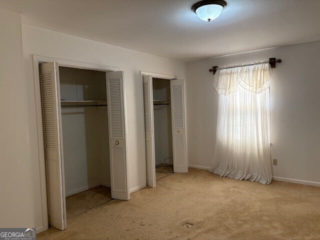 unfurnished bedroom featuring light carpet, baseboards, and two closets