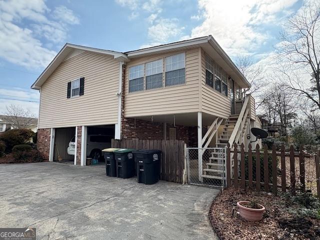 rear view of house featuring a garage, concrete driveway, stairs, fence, and brick siding