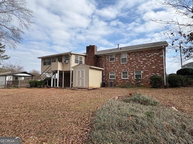 rear view of house featuring brick siding, a chimney, fence, a shed, and an outdoor structure