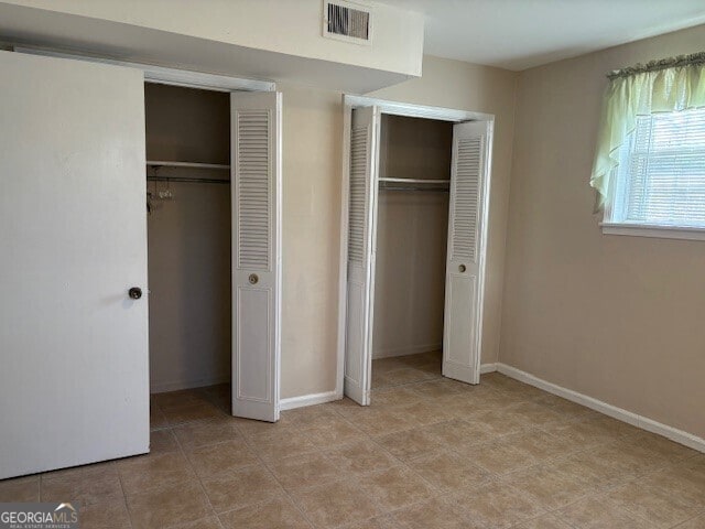 unfurnished bedroom featuring baseboards, visible vents, and multiple closets