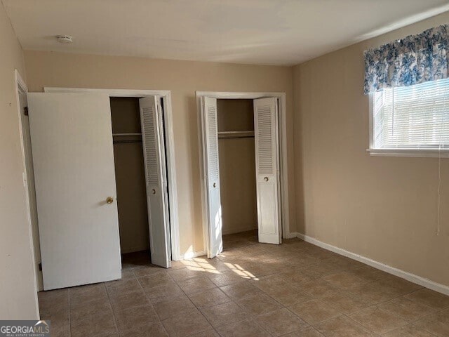 unfurnished bedroom with multiple closets and baseboards