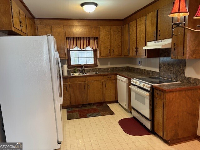 kitchen with white appliances, brown cabinetry, light floors, under cabinet range hood, and a sink