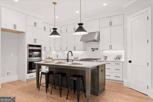 kitchen with white cabinets, appliances with stainless steel finishes, a kitchen island with sink, and wall chimney range hood