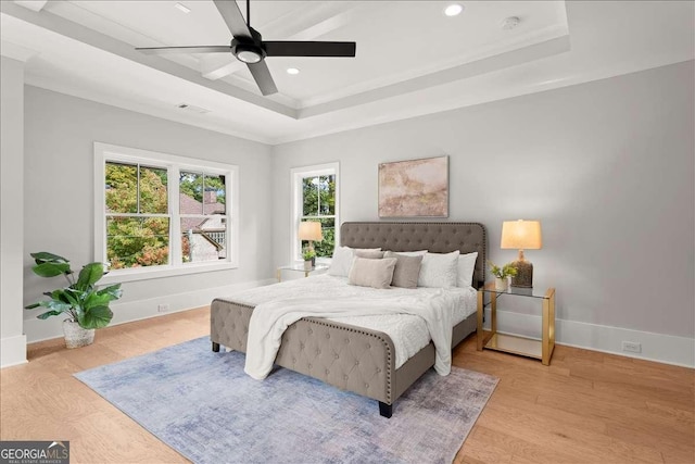 bedroom with ceiling fan, light hardwood / wood-style floors, and a tray ceiling