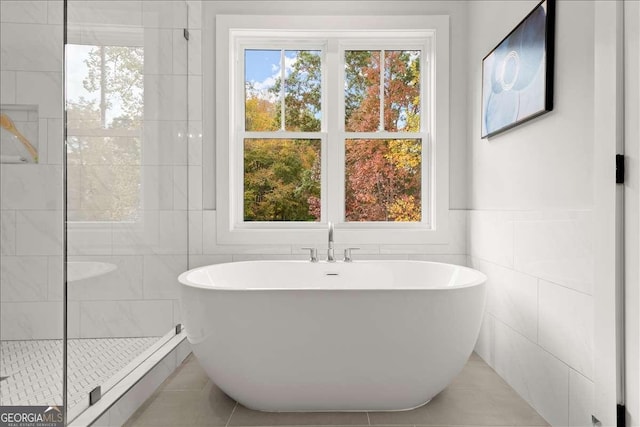 bathroom with tile patterned floors, independent shower and bath, tile walls, and a wealth of natural light