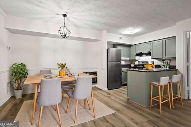 kitchen featuring hanging light fixtures, wood-type flooring, stainless steel appliances, and a textured ceiling