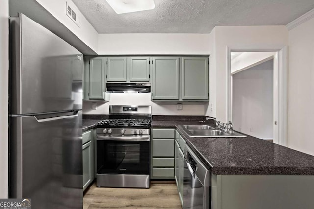 kitchen featuring sink, dark stone countertops, stainless steel appliances, light hardwood / wood-style floors, and a textured ceiling