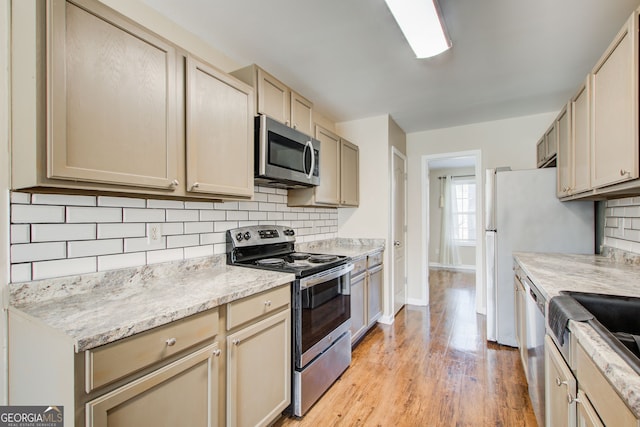 kitchen featuring appliances with stainless steel finishes, backsplash, light stone counters, cream cabinets, and light wood-type flooring