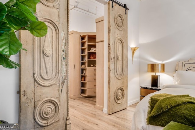 bedroom with a spacious closet, a barn door, and light wood-type flooring