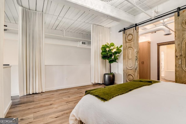 bedroom featuring hardwood / wood-style floors, beam ceiling, and a barn door