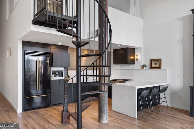 kitchen featuring light hardwood / wood-style flooring, a towering ceiling, a kitchen breakfast bar, kitchen peninsula, and built in fridge