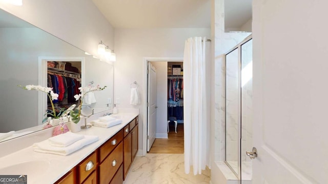 bathroom with marble finish floor, double vanity, a spacious closet, and an enclosed shower