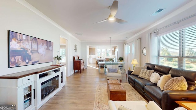 living room with light wood-style flooring, visible vents, ceiling fan, and ornamental molding