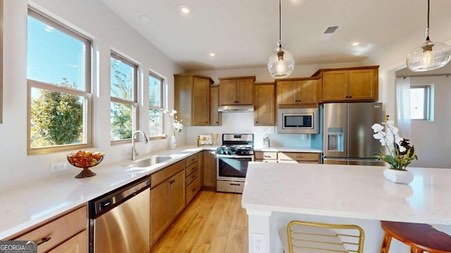 kitchen featuring under cabinet range hood, a sink, appliances with stainless steel finishes, brown cabinets, and pendant lighting