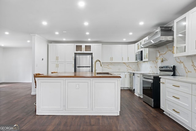 kitchen with appliances with stainless steel finishes, a kitchen island with sink, white cabinets, and range hood