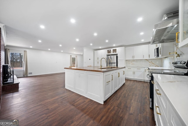 kitchen with dark wood-type flooring, appliances with stainless steel finishes, an island with sink, white cabinets, and backsplash