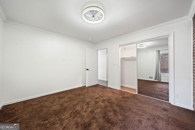 unfurnished bedroom with dark carpet, ornamental molding, and a closet