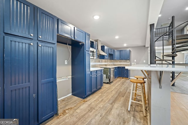 kitchen featuring wall chimney range hood, light hardwood / wood-style flooring, a breakfast bar, and blue cabinets