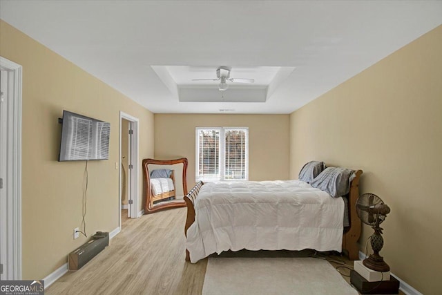 bedroom with ceiling fan, a tray ceiling, and light wood-type flooring