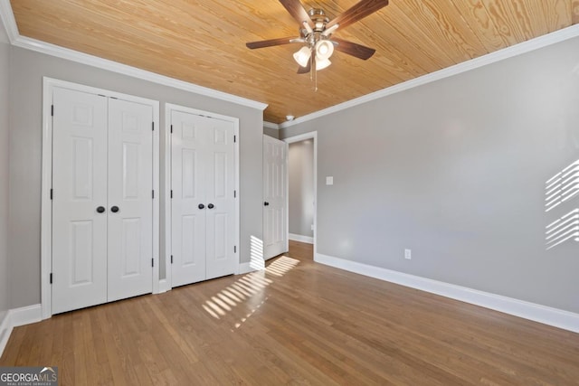 unfurnished bedroom featuring ceiling fan, hardwood / wood-style floors, ornamental molding, two closets, and wooden ceiling