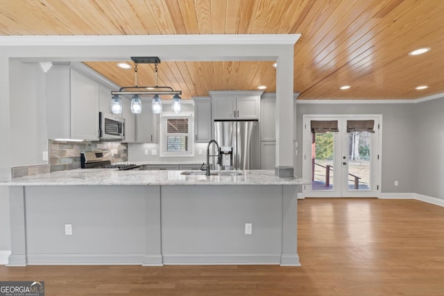 kitchen featuring pendant lighting, sink, kitchen peninsula, stainless steel appliances, and light stone countertops