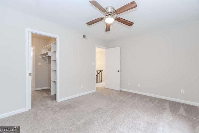 unfurnished bedroom with ceiling fan, a walk in closet, and light colored carpet