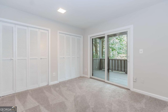 unfurnished bedroom with two closets, light carpet, and access to outside