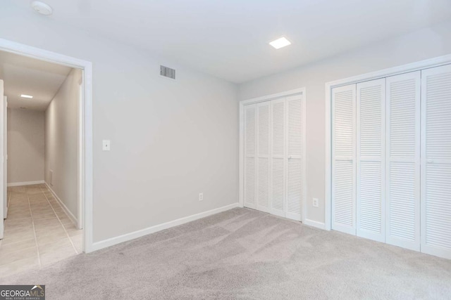 unfurnished bedroom with light carpet and multiple closets