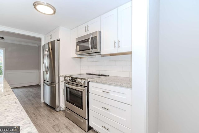 kitchen featuring light hardwood / wood-style flooring, appliances with stainless steel finishes, white cabinetry, backsplash, and light stone counters