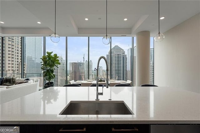 kitchen with sink, hanging light fixtures, a raised ceiling, light stone countertops, and a center island with sink