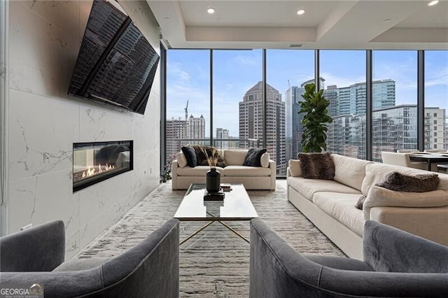 living room with a premium fireplace, a wall of windows, a raised ceiling, and plenty of natural light