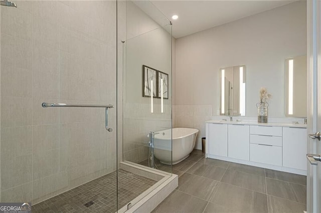 bathroom featuring independent shower and bath, vanity, tile walls, and tile patterned floors