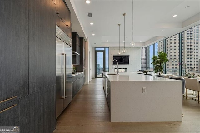 kitchen featuring pendant lighting, sink, built in refrigerator, a spacious island, and light hardwood / wood-style floors