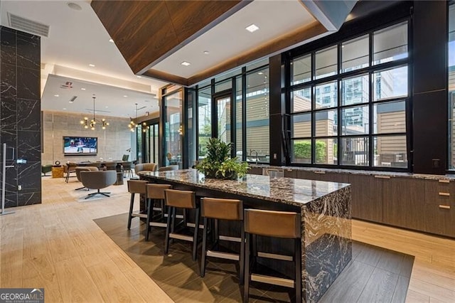 bar with tile walls, dark stone countertops, dark brown cabinetry, an inviting chandelier, and light hardwood / wood-style flooring