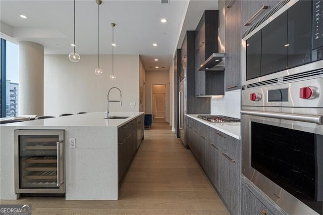 kitchen featuring wine cooler, sink, hanging light fixtures, appliances with stainless steel finishes, and an island with sink