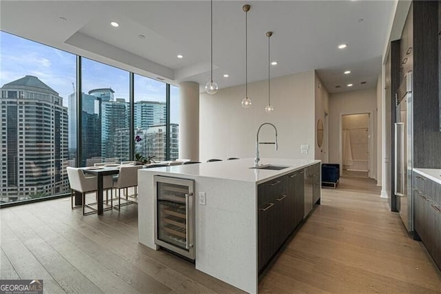 kitchen with pendant lighting, sink, wine cooler, light hardwood / wood-style floors, and an island with sink